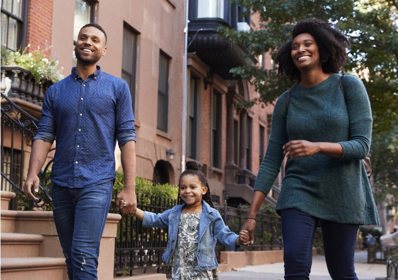 a young family holding hands and waking down a street