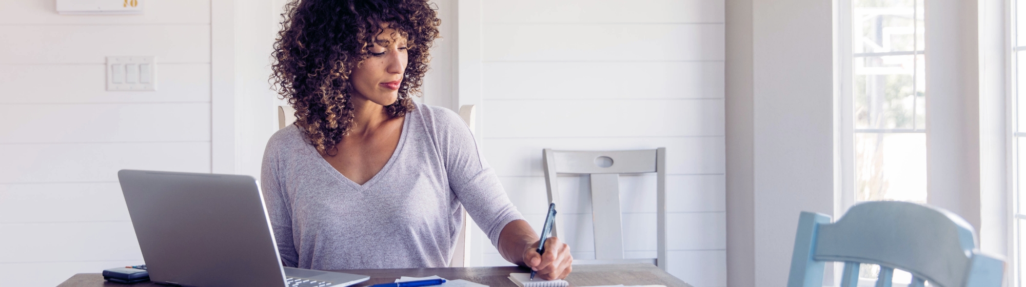 Woman sits at her dining room table with laptop and financial reports