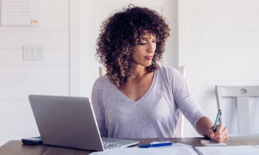 Woman sits at her dining room table with laptop and financial reports