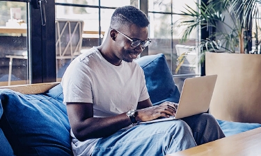 young man using his cash back debit card on his computer from his couch