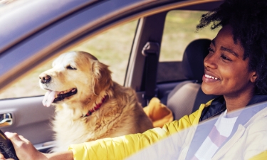 Young woman driving with her dog in the front passenger seat