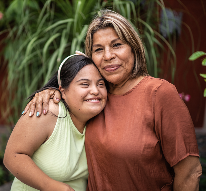 A woman embracing her smiling daughter with Down syndrome in a garden setting
